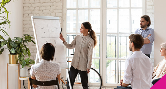 a woman writing on a flipchart in front of coworkers in a relaxed office